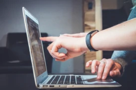 Recorte de uma imagem mostrando um notebook com duas pessoas conversando e uma delas apontando na tela do notebook